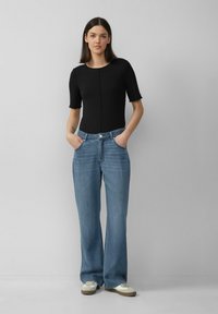 Zwarte korte mouwen bodysuit gecombineerd met lichtblauwe, wijde spijkerbroek met knoopsluiting en voorzakken. Casual sneakers maken de look af.