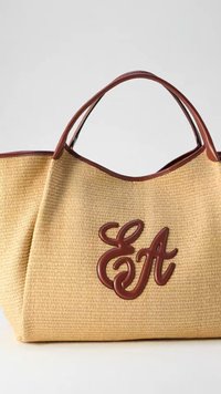 Μπεζ πλεκτή τσάντα tote με καφέ δερμάτινα χερούλια και καφέ δερμάτινα αρχικά '"EA"' μπροστά, τοποθετημένη σε απλό φόντο.