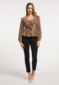 Bluse med leopardprint og flæser ved halsudskæringen og ærmerne, parret med sorte tætsiddende bukser og nude højhælede sko. Glat stof, flagrende talje.