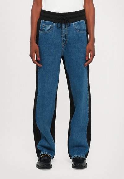 Pantalon en denim avec une taille élastique noire, des panneaux latéraux et une coupe décontractée. Le tissu est bleu clair avec une finition texturée.
