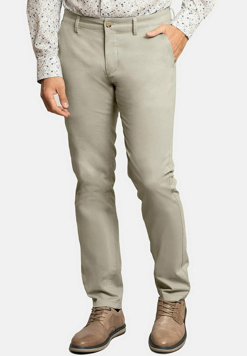 Pantalones beiges de tela suave con corte ajustado, que cuentan con un bolsillo frontal, cierre de botón, y se combinan con zapatos marrones.