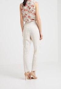 Beżowe spodnie z wysokim stanem o teksturowanym wykończeniu, połączone z bezrękawnikową bluzką w kwiaty i nagimi sandałami na wysokim obcasie.