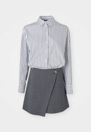 Chemise à boutonner avec de fines rayures verticales bleues et blanches, accompagnée d'une jupe portefeuille grise avec un bouton décoratif sur le côté gauche.
