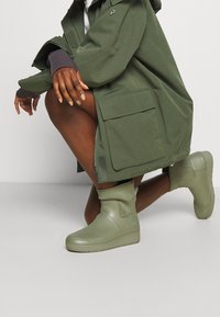 Bottes d"avalanche vertes imperméables à la texture lisse, bout arrondi et détail de logo subtil sur le côté, assorties à un manteau vert assorti.