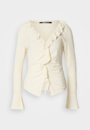 Blusa de manga longa creme com decote em V, acabamento com babados, lado franzido e mangas em forma de sino. Feita de um tecido leve e texturizado.