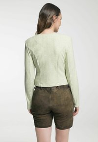 Hellgrünes, geripptes Langarmoberteil mit figurbetontem Design und Rundhalsausschnitt, kombiniert mit braunen Wildleder-Shorts. Details umfassen Nähte und Textur.