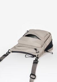 Grauer Stoff-Rucksack mit schlankem Design, der über zwei mit Reißverschlüssen verschlossene Fächer, verstellbare Trageriemen und Hardwareakzente verfügt. Flach und modern.