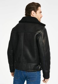 Czarna skórzana kurtka z fakturowanym, puszystym kołnierzem i detalami wzdłuż szwów na ramionach. Posiada regulowany pasek w talii oraz dopasowany krój.