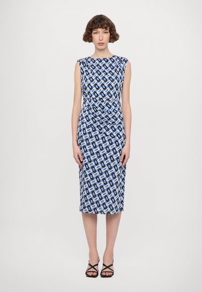 Vestido azul y blanco con un diseño estampado, silueta ajustada, sin mangas, a la altura de la rodilla y con detalles fruncidos en los lados. Combinado con tacones negros con tiras.