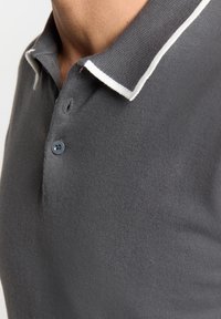 Grijze polo shirt gemaakt van gebreide stof, met een kraag met witte strepen en een blauwe knoop. Close-up van de stofstructuur en het ontwerp van de kraag.