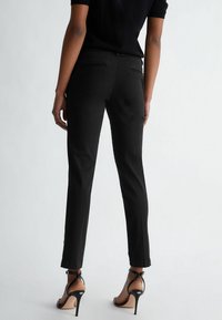 Czarne dopasowane spodnie o gładkiej fakturze, zwężające się nogawki i dyskretne tylne kieszenie, w połączeniu z czarnymi sandałkami na wysokim obcasie z paskami.