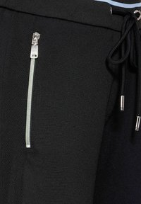 Svarta träningsbyxor med en dragkedjeficka och silverdetalj, dragsko i midjan med metallspetsar och texturerad tyg.