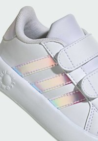 Zapatilla blanca con parte superior sintética, que presenta rayas iridiscentes, lengua texturizada y cierres de tira de velcro. Suela sólida de goma.