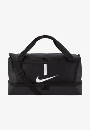 Sac de sport noir Nike avec des compartiments à double fermeture éclair, une sangle d'épaule réglable, et un logo blanc bien visible sur le devant. Construction en tissu durable.