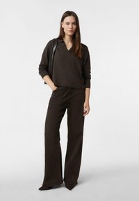 Brązowy, oversize sweter z dekoltem w serek w połączeniu z pasującymi, wysokim stanem i szerokimi nogawkami spodniami. Gładka tkanina i płaskie szwy. Szpilki z ostro zakończonym noskiem.