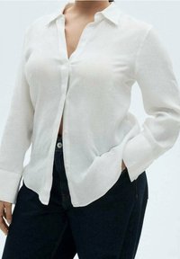 Chemise blanche en lin à boutons, col, manches longues et coupe décontractée, associée à un jean denim foncé.