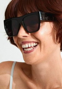 Black oversized sunglasses with thick frames and dark lenses. The frames have glossy accents. The background is neutral.