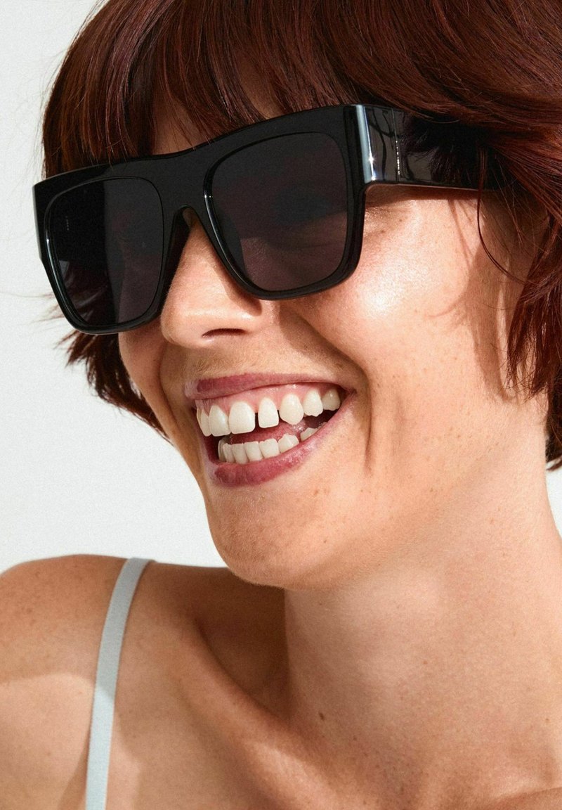 Black oversized sunglasses with thick frames and dark lenses. The frames have glossy accents. The background is neutral.