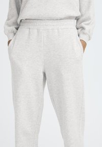 Svetlo šedé tepláky s jemnou textúrou, elastickým pásom, bočnými vreckami a zúženými nohavicami s jemným švom.