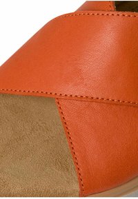 Sandale en cuir orange avec des bretelles croisées ; elle présente une semelle intérieure beige douce et des coutures subtiles le long des bords pour le détail.
