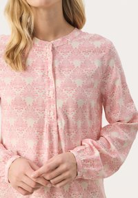 Lyserød bluse med lange ærmer og et let blomstermønster, med rund udkæring og knaplukning foran. Blødt, let stof.