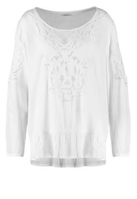 Blouse blanche à manches longues avec broderie florale sur la poitrine et les manches et détail volanté à l'ourlet.