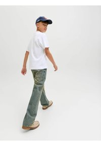 Bílý bavlněný tričko, světle modré rozšířené džíny se zeslabeným praním a béžová obuv. Námořnická čepice dotváří outfit. Jednoduchý design, neformální styl.