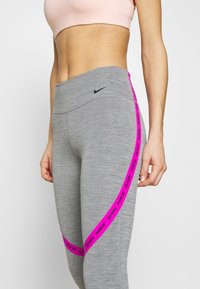 Grå leggins med høj talje, der er accentueret af et lyserødt Nike-logo bånd langs siden, lavet af strækbart stof.