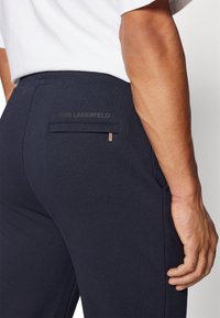 Pantaloni blu navy realizzati in un tessuto morbido, con una tasca posteriore che presenta un logo discreto. Il design include una texture liscia e una vestibilità su misura.