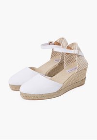 White canvas espadrilles with a woven jute wedge heel, ankle strap, and textured back panel. Soft interior lining and rubber sole detail.