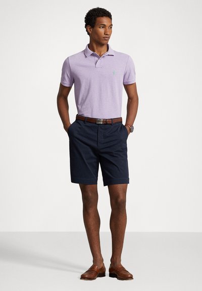Hele lilla polo särk väikese logoga, mis on kombineeritud tumedate navy värvi lühikeste pükstega. Pruun nahkrihm ja kingad täiustavad juhuslikku välimust.