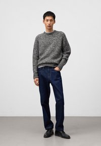 Szary sweter z dzianiny o okrągłym dekolcie, w połączeniu z ciemnoniebieskimi dżinsami i czarnymi butami. Prosty, luźny krój z fakturowanym materiałem.