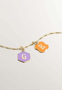 Collar de cadena dorada con dos colgantes de esmalte, uno en forma de hexágono púrpura con la letra G y otro en forma de escudo naranja con la letra R.