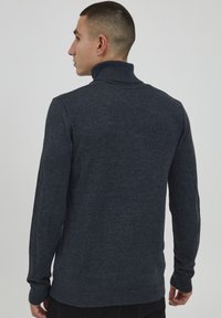Sötét szürke kötött garbó, bordás gallérral, hosszú ujjakkal és testhezálló fazonnal, sima textúrával és minimalista stílussal.