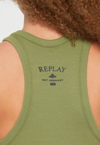 Λαδί πράσινη ριμπ αμάνικη μπλούζα με στρογγυλή λαιμόκοψη και σχέδιο racerback. Διαθέτει τυπωμένο μαύρο λογότυπο με την επιγραφή "REPLAY NOT ORDINARY."