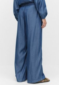 Jeans med vida ben och elastisk midja, i en djupblå färg, med en mjuk yta och lös passform, kombinerat med sandaler.