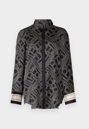 Chemise noire à manches longues avec un motif géométrique blanc, un col, une patte de boutonnage et des accents rayés contrastants sur les poignets.