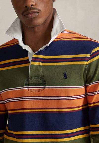 Πολύχρωμο ριγέ πουκάμισο ράγκμπι με πορτοκαλί, πράσινες, ναυτικές και κίτρινες ρίγες. Λευκός γιακάς με κεντημένο λογότυπο και διακοσμητική ραφή.