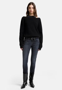 Czarny sweter z dzianiny z odsłoniętymi ramionami, połączony z ciemnymi, dopasowanymi jeansami i czarnymi botkami na obcasie. Gładka faktura i dopasowana sylwetka.