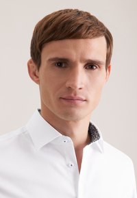 Camicia bianca con colletto a contrasto decorato da un motivo. Caratterizzata da un design con bottoni e una vestibilità aderente. Tessuto dalla texture liscia.