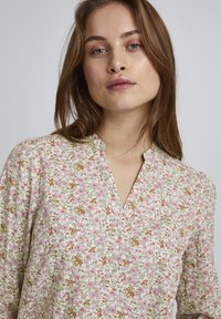 Blomstret bluse med en cremefarvet baggrund, prydet med pink og grønne mønstre, en V-udskæring og rynkede ærmer for ekstra tekstur.
