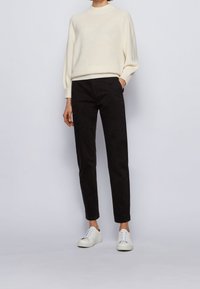 Jersey de punto crema con un cuello alto, pantalones negros ajustados y zapatillas blancas. El atuendo presenta un corte relajado y texturas suaves.