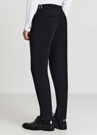 Schwarze, maßgeschneiderte Hose mit glatter Textur, ausgestattet mit Seitentaschen und einem Gürtelösenakzent. Kombiniert mit polierten schwarzen Schuhen.