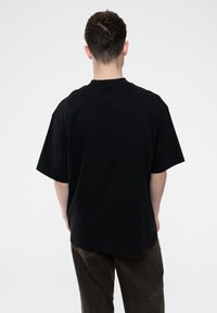 Black cotton t-shirt with short sleeves, relaxed fit, and a crew neckline. Back view shows a solid color with no visible patterns or embellishments.