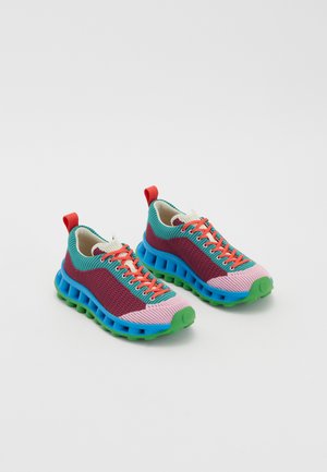 Kleurige sneakers met een gebreide bovenkant in roze, paars en turquoise, een groene zool, oranje veters en een rode hieltab.