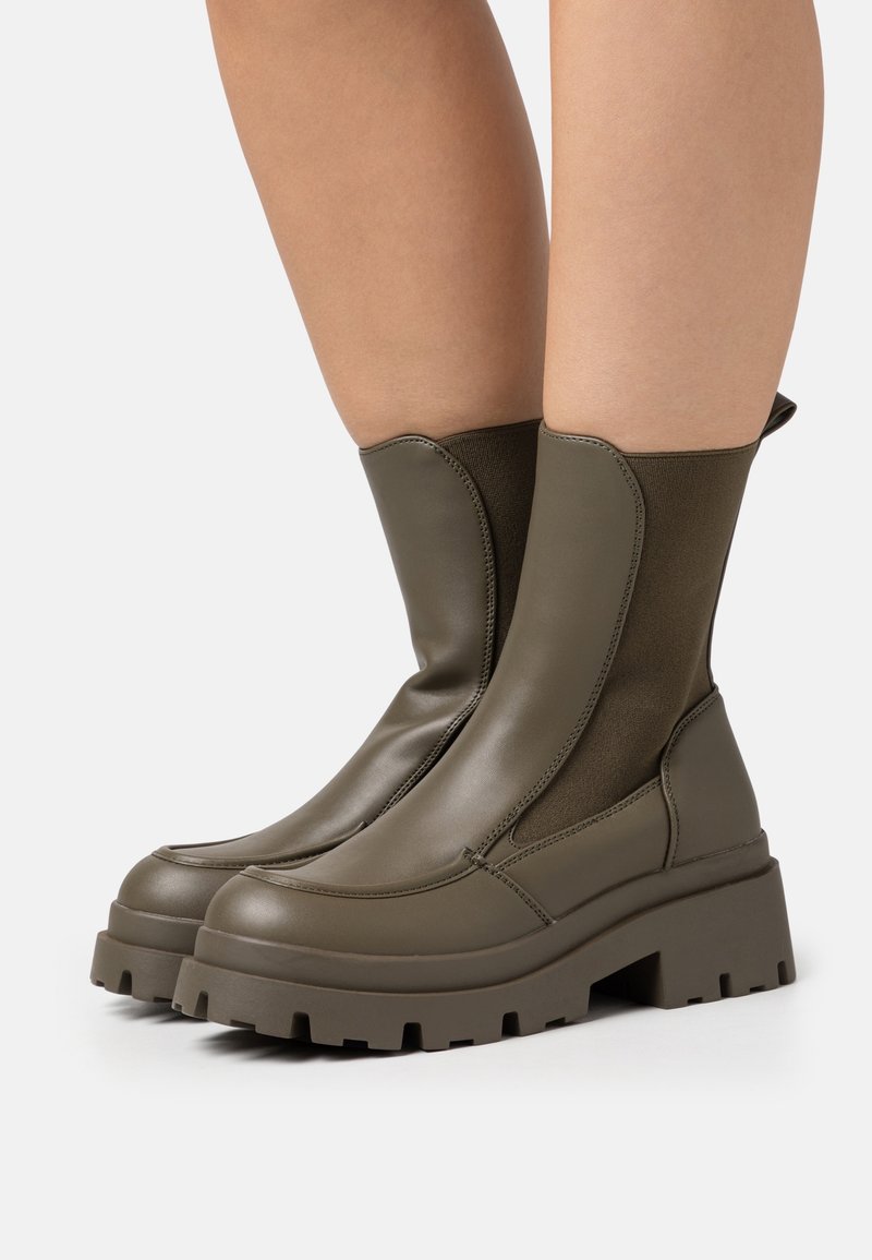 Botas de tobillo verde oliva con un acabado de cuero elegante, paneles laterales elásticos, suelas de plataforma de goma gruesa y un diseño de punta redonda.