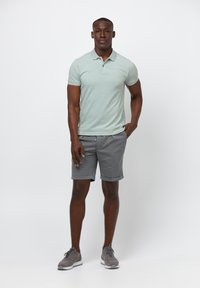 Ljust grön kortärmad polo med krage, tillsammans med grå shorts. Shortsen är uppvikta och har dragsko i midjan.