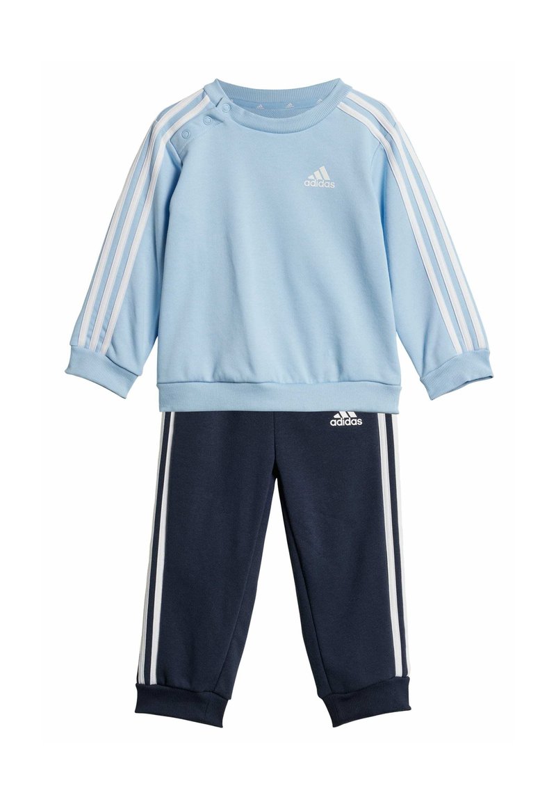 Felpa azzurro chiaro con bottoni bianchi sulle spalle, con tre strisce bianche sulle maniche; abbinata a pantaloni jogger blu navy con strisce coordinate.