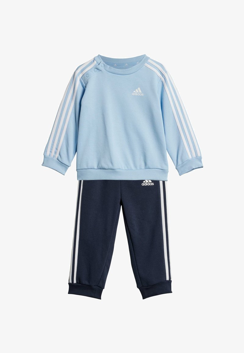 Felpa azzurro chiaro con bottoni bianchi sulle spalle, con tre strisce bianche sulle maniche; abbinata a pantaloni jogger blu navy con strisce coordinate.