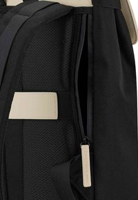 Czarny plecak z teksturowanej tkaniny, wyposażony w boczną kieszeń na suwak, lekki design i kontrastowy kremowy pasek.